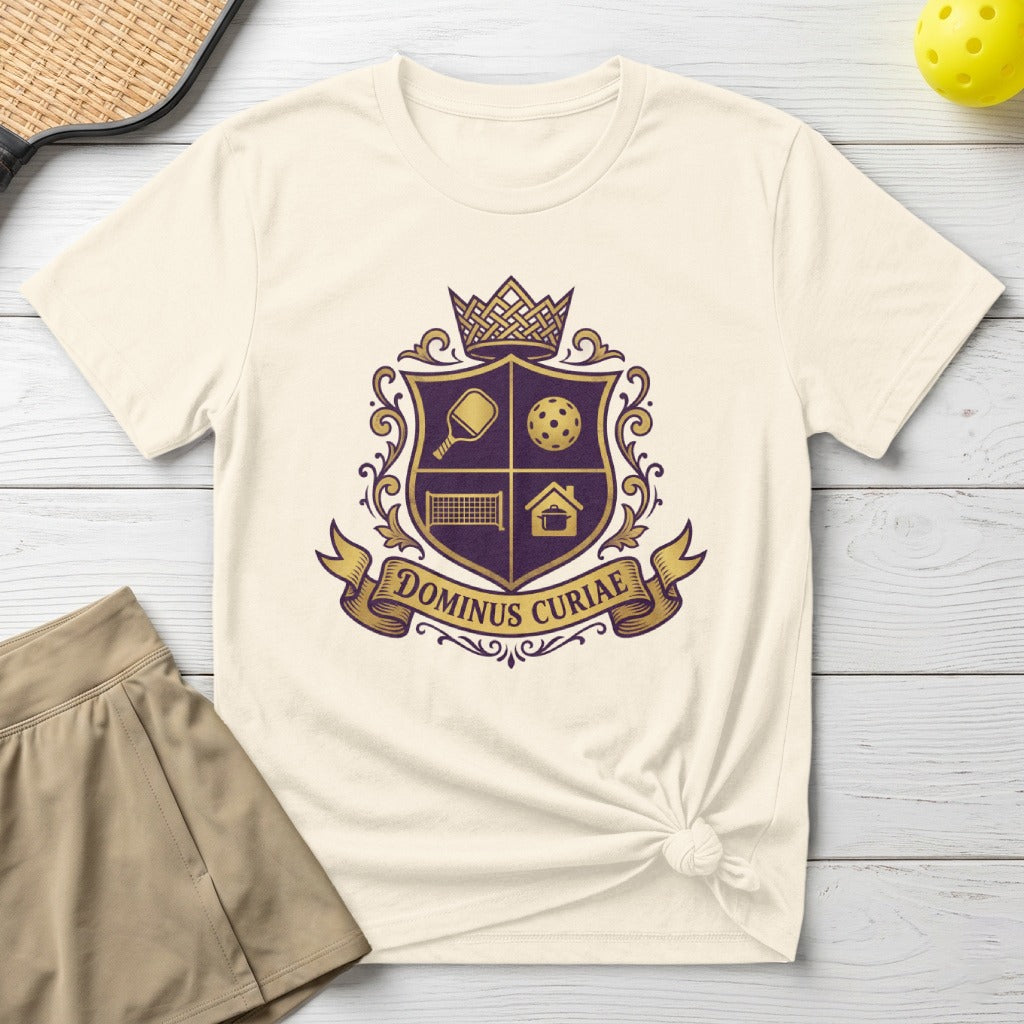 Cream t-shirt with purple shield logo featuring pickleball and house icons and text.