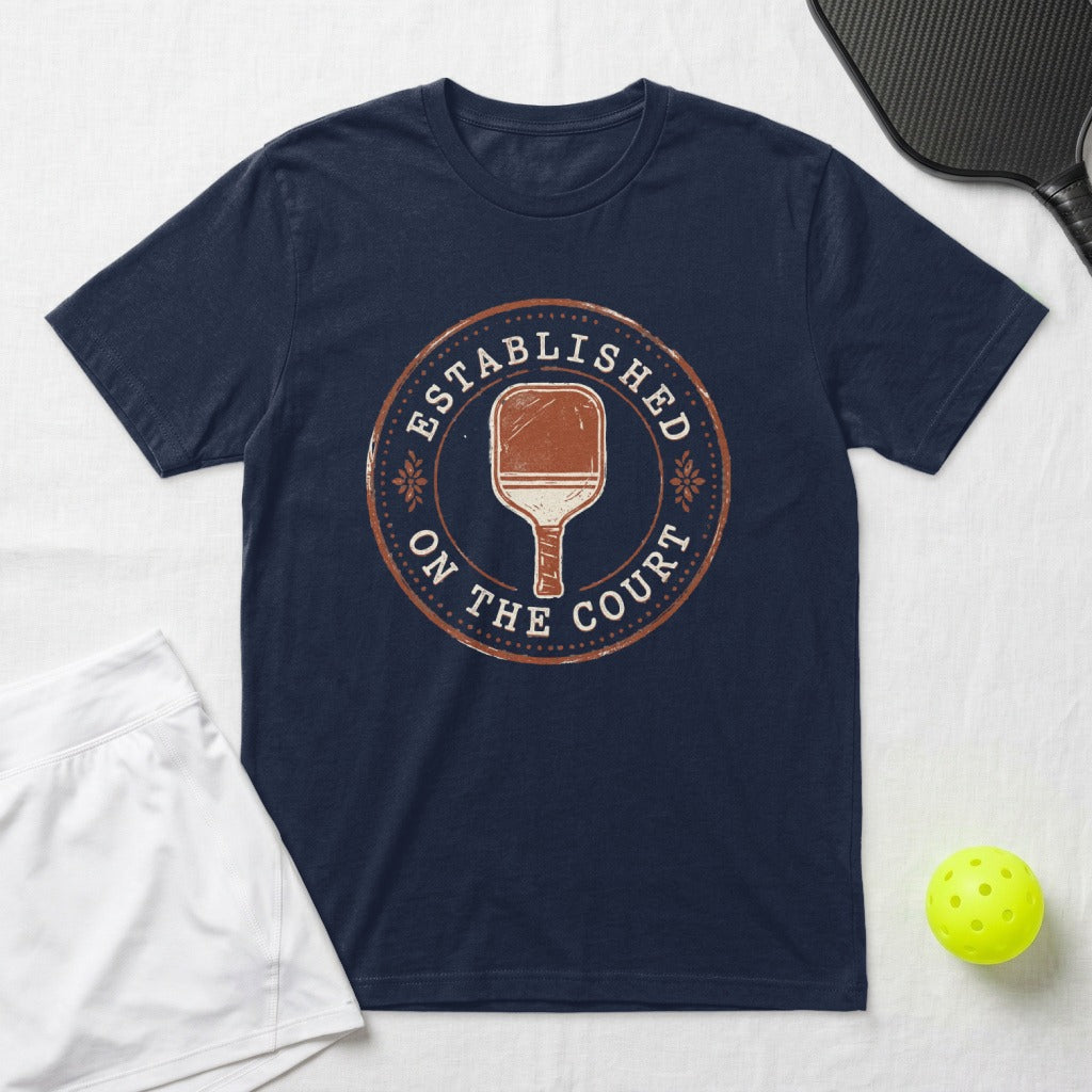 Navy t-shirt with circular "Established on the Court" pickleball graphic.