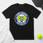 Black t-shirt with a circular logo featuring pickleball paddles, balls, and text.