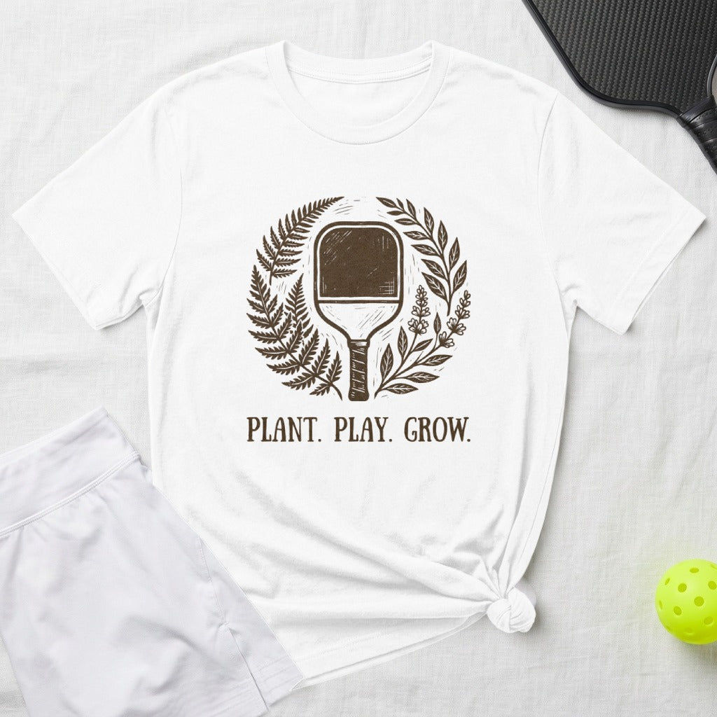 White t-shirt with pickleball paddle and plant design, saying "PLANT. PLAY. GROW."