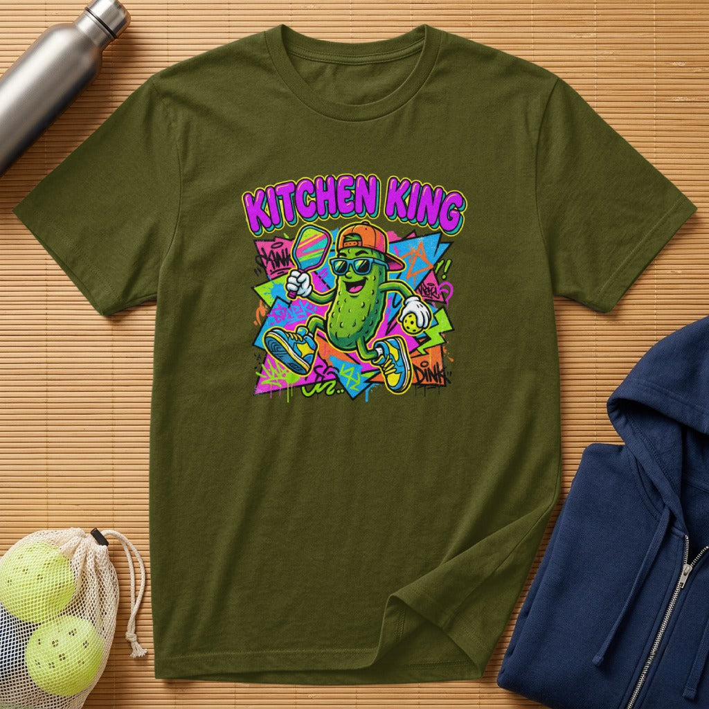 Green t-shirt featuring a cartoon pickle playing pickleball with graffiti background.