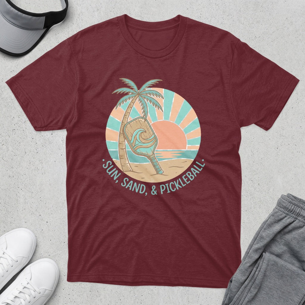 Maroon t-shirt with a circular graphic of a pickleball paddle on a beach at sunset.
