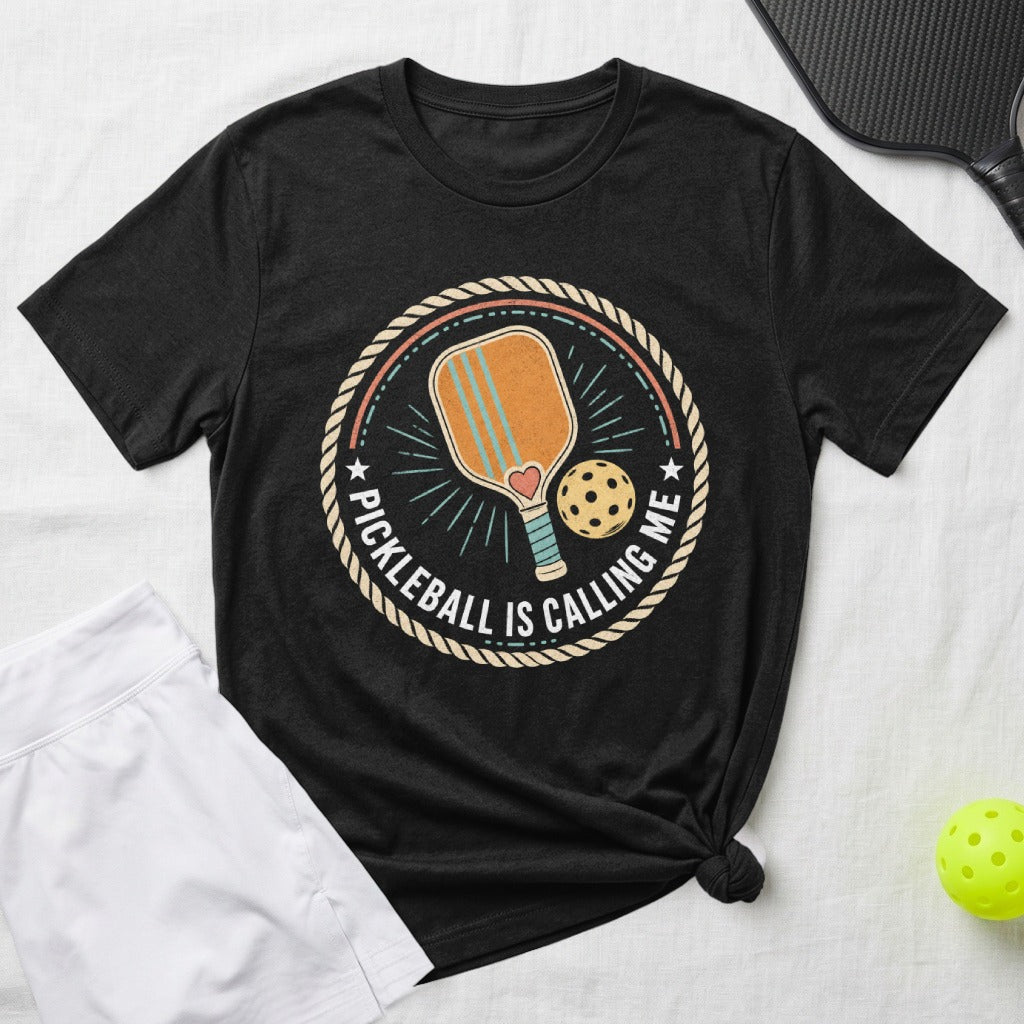 Black t-shirt with pickleball graphic and text "PICKLEBALL IS CALLING ME".