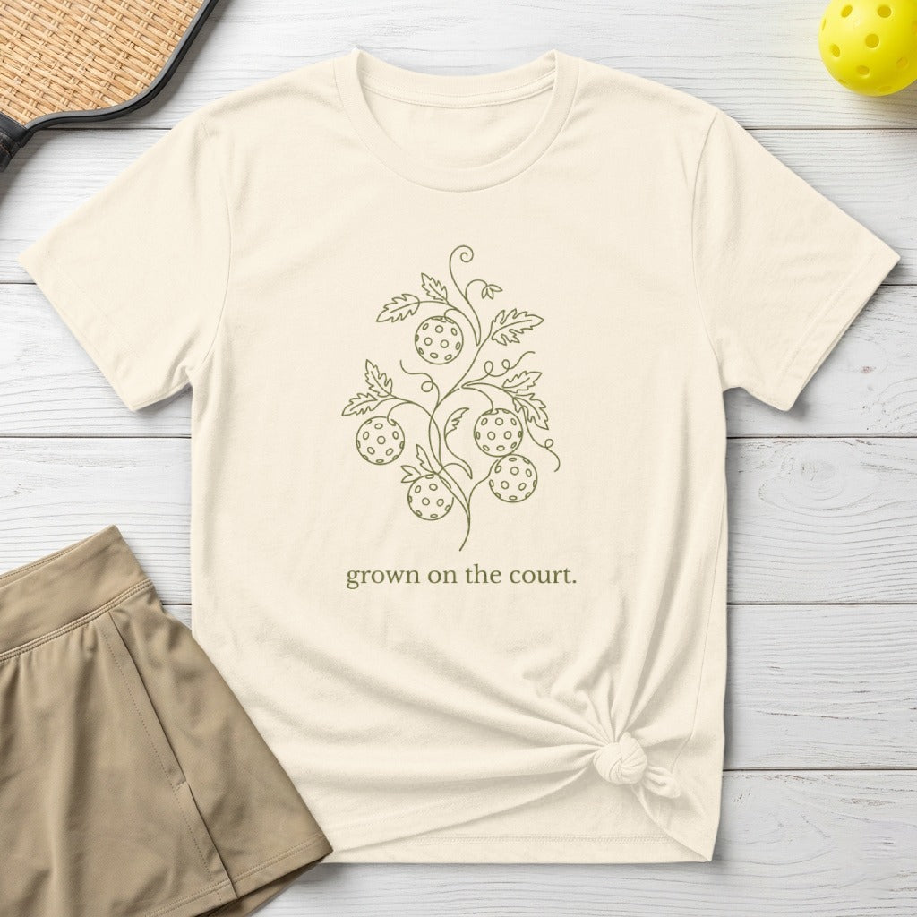 Cream t-shirt with a minimalist pickleball vine design and text "grown on the court."