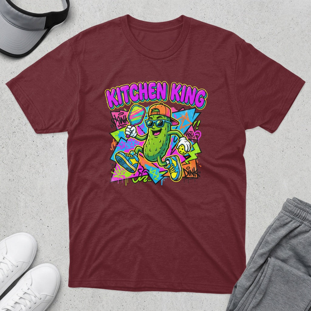 Maroon t-shirt featuring a cartoon pickle playing pickleball, text reads "Kitchen King".