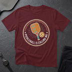 Maroon t-shirt with a circular graphic showing a pickleball paddle, ball, and the text "Pickleball is Calling Me".
