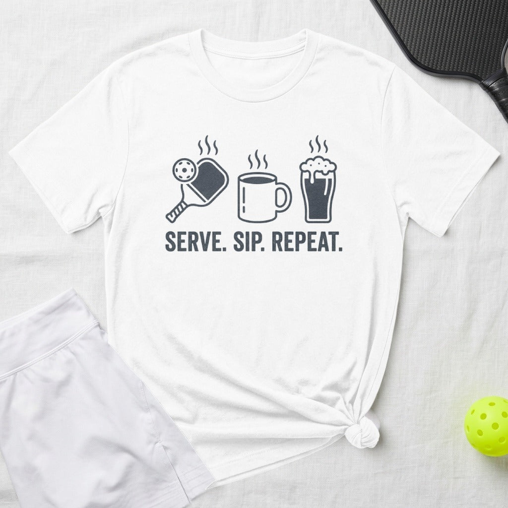 White t-shirt with graphic of pickleball, coffee cup, beer mug, and text "Serve. Sip. Repeat."