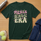 Dark green t-shirt with "Pickle Ball Era" text in pink and cream.