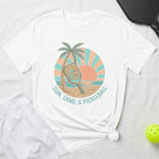 White t-shirt with a circular graphic of a pickleball paddle, palm tree, and sun.