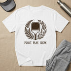 White t-shirt with pickleball paddle and plant design, "PLANT. PLAY. GROW." text.