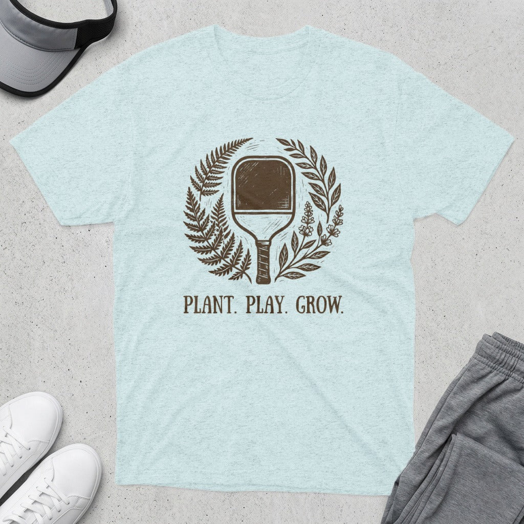 Light blue t-shirt with a pickleball paddle and floral wreath, text reads PLANT. PLAY. GROW.