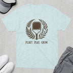 Light blue t-shirt with a pickleball paddle and floral wreath, text reads PLANT. PLAY. GROW.