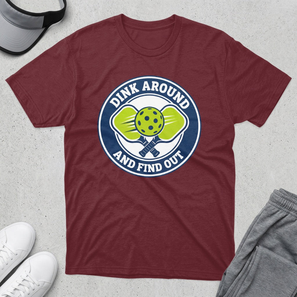 Burgundy t-shirt with a circular logo featuring pickleball paddles and balls, and text "Dink Around and Find Out".