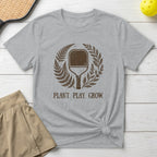 Gray t-shirt with "PLANT. PLAY. GROW." and a pickleball paddle within ferns.