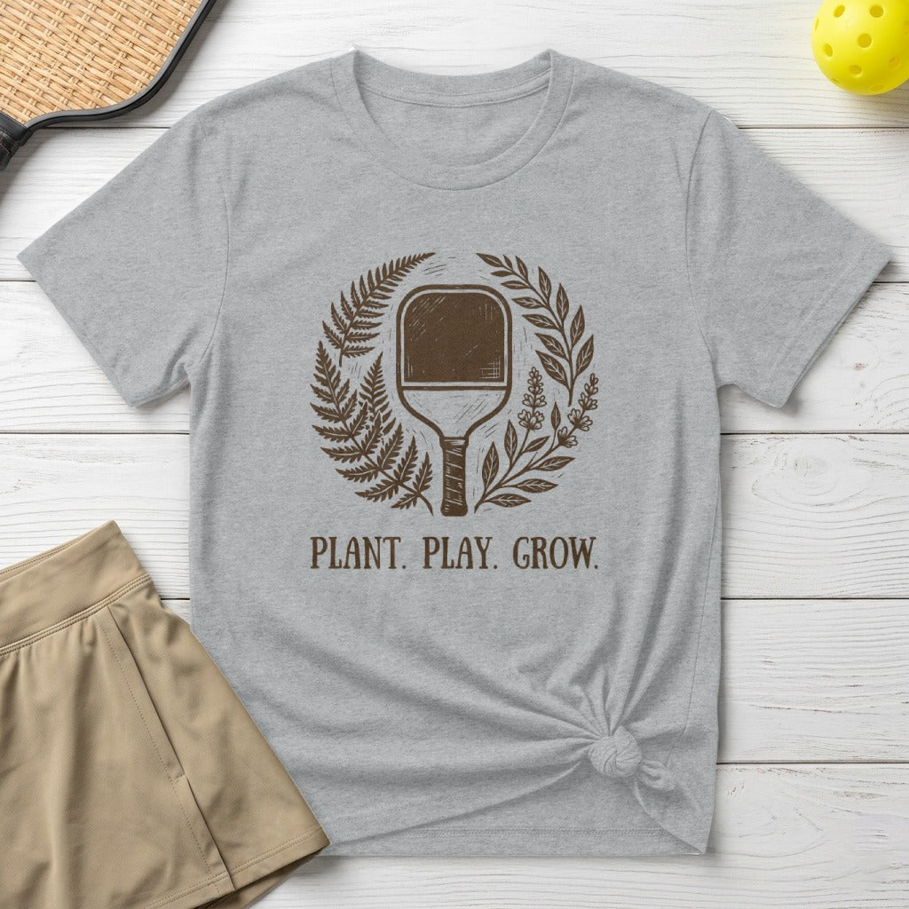 Gray t-shirt with "PLANT. PLAY. GROW." and a pickleball paddle within ferns.