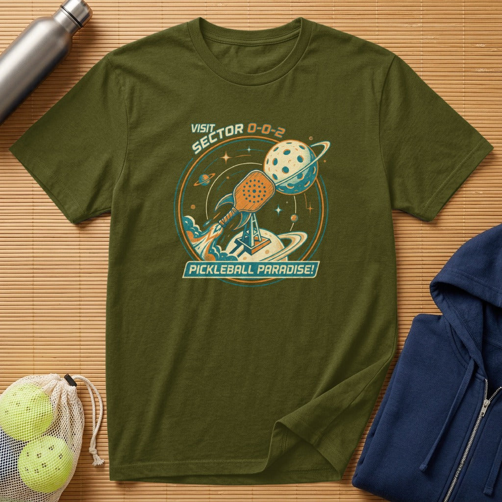 Olive t-shirt with "Pickleball Paradise" text and a rocket ship to a pickleball planet.