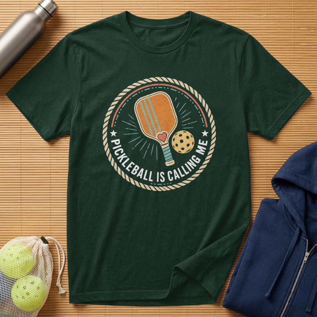 Dark green t-shirt with circular "Pickleball is Calling Me" graphic featuring a paddle and ball.