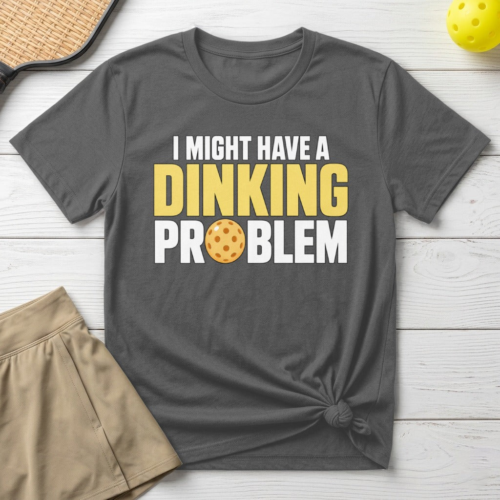 Dark grey t-shirt with yellow and white text reading "I MIGHT HAVE A DINKING PROBLEM" and a pickleball.