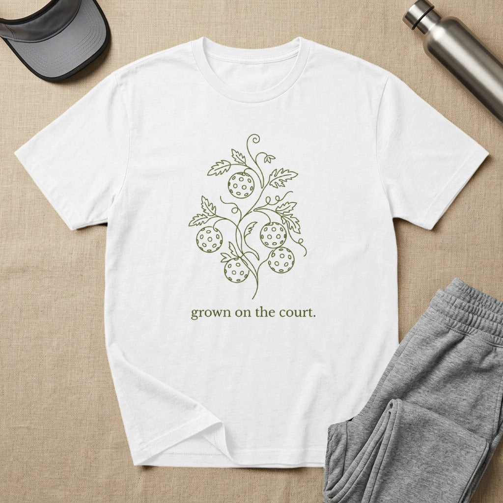 White t-shirt with green line art of pickleballs and vine, text "grown on the court".