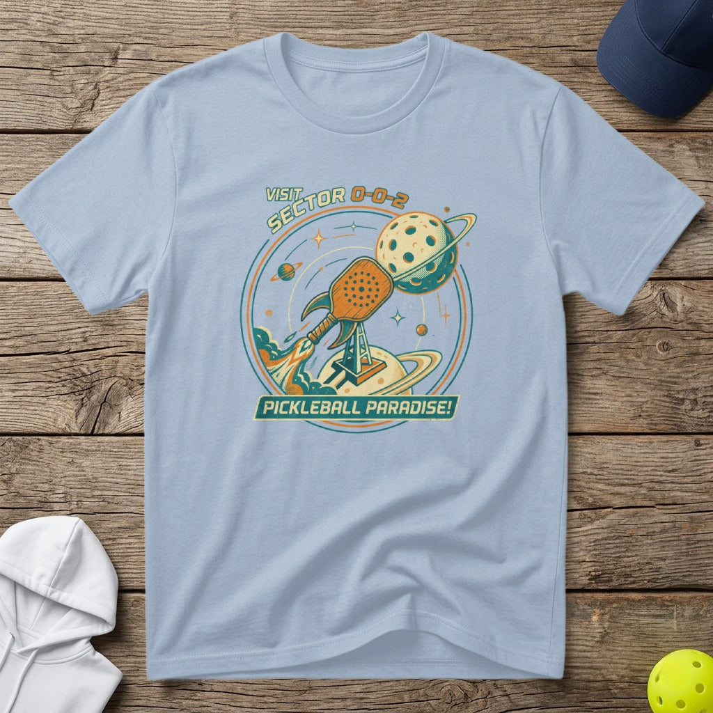 Light blue t-shirt with "Pickleball Paradise" text and rocket launching a pickleball.