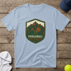 Light blue t-shirt with "Pickleball Trailblazers" shield logo featuring a pickleball and crossed paddles.