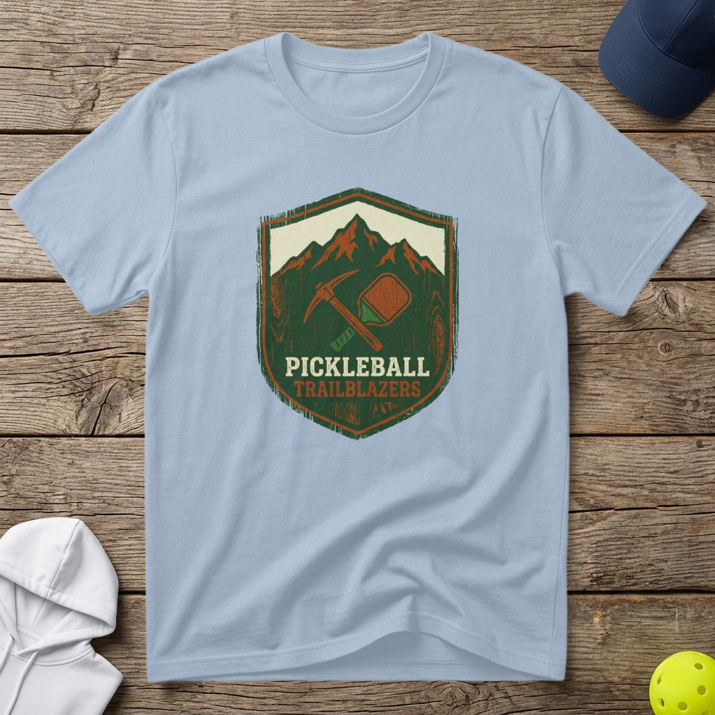 Light blue t-shirt with "Pickleball Trailblazers" shield logo featuring a pickleball and crossed paddles.