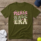 Olive green t-shirt with "Pickle Ball Era" text in bubble font.