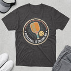 Dark grey t-shirt with a pickleball paddle, ball, and text "Pickleball is Calling Me".