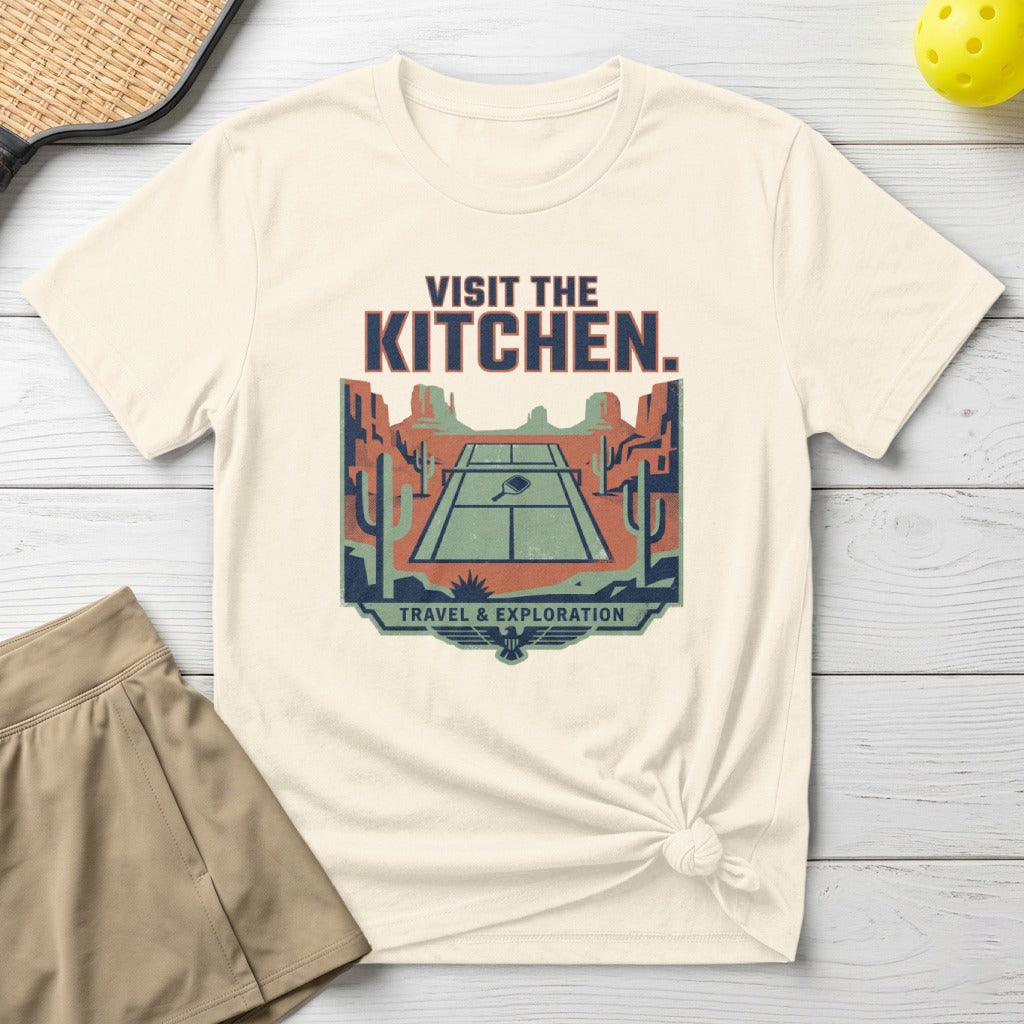 T-shirt graphic: pickleball court in desert with "VISIT THE KITCHEN." text.